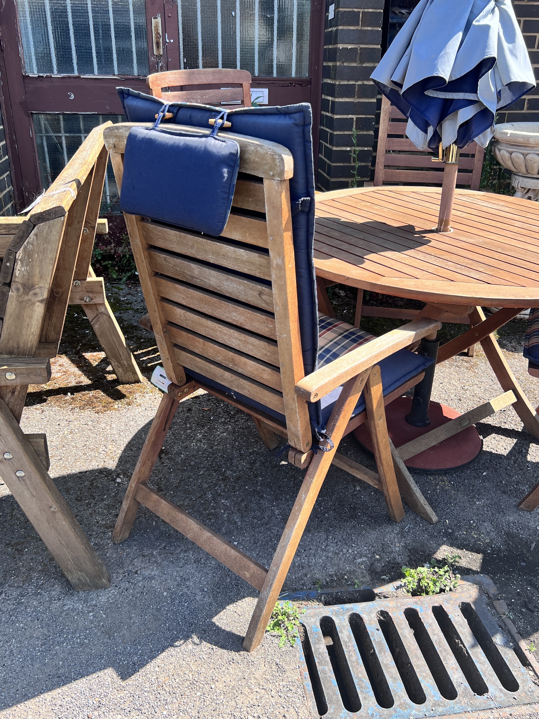 A Royal Craft teak folding table and four chairs with two cushions, parasol and cast metal base, table 110cm diameter, height 74cm.